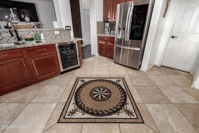 kitchen with light stone counters, a sink, wine cooler, stainless steel fridge, and light tile patterned floors