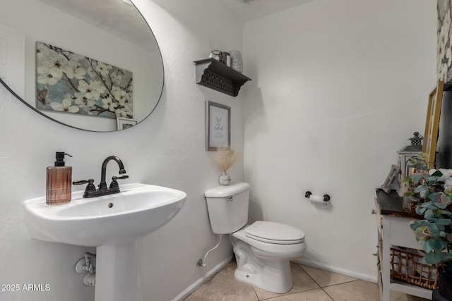 half bath with tile patterned floors, baseboards, toilet, and a sink