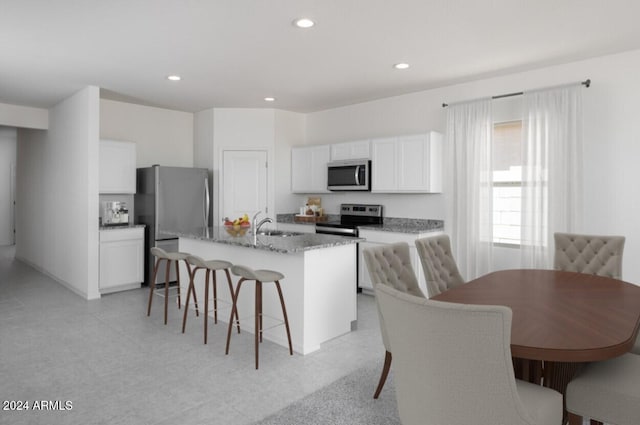 kitchen featuring appliances with stainless steel finishes, light stone counters, a kitchen island with sink, white cabinets, and a breakfast bar area