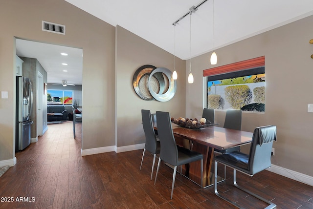 dining area featuring rail lighting, dark wood-type flooring, and lofted ceiling