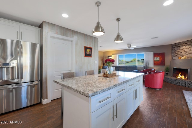 kitchen with stainless steel fridge with ice dispenser, a large fireplace, a center island, and white cabinetry