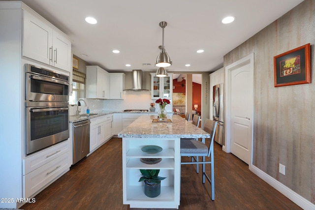 kitchen with sink, wall chimney exhaust hood, decorative light fixtures, a kitchen island, and stainless steel appliances