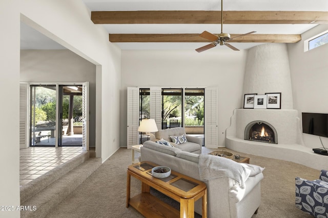 living room featuring ceiling fan, a fireplace, beamed ceiling, and light colored carpet