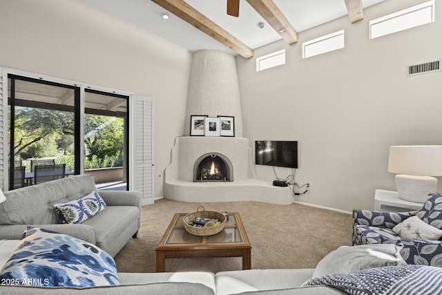 living room with ceiling fan, a large fireplace, a high ceiling, beamed ceiling, and carpet floors