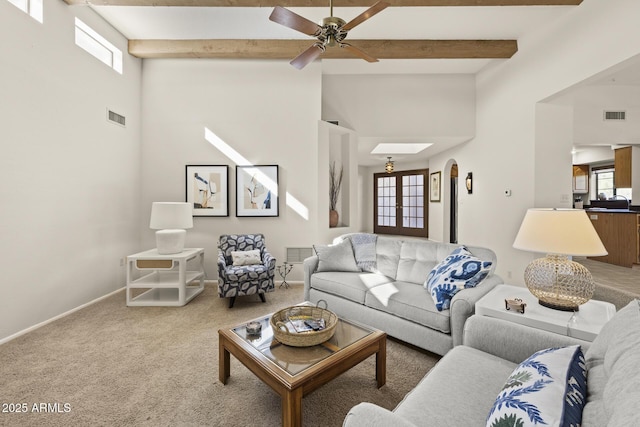 carpeted living room with ceiling fan, beam ceiling, a high ceiling, and a skylight