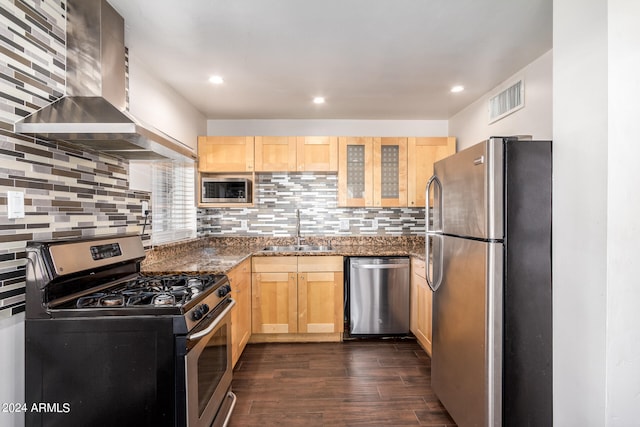 kitchen with appliances with stainless steel finishes, dark stone countertops, wall chimney exhaust hood, dark hardwood / wood-style floors, and sink