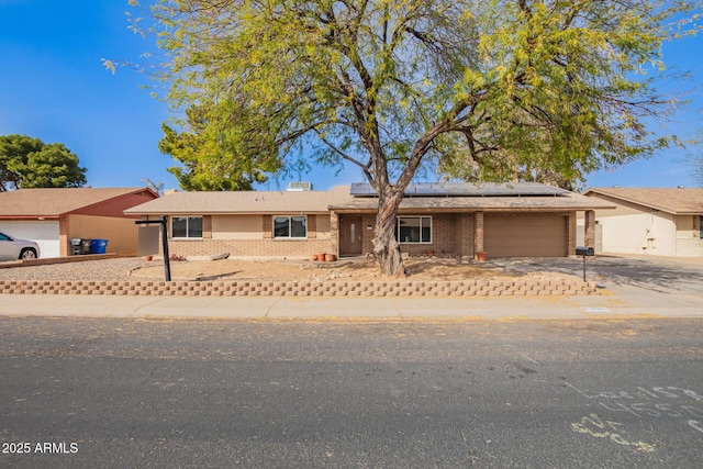 single story home featuring an attached garage, driveway, brick siding, and solar panels