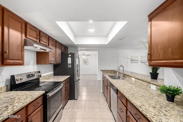 kitchen with a raised ceiling, appliances with stainless steel finishes, a sink, ceiling fan, and under cabinet range hood