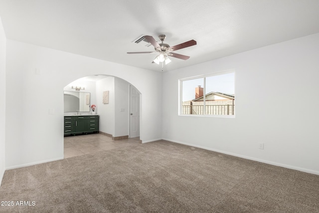 unfurnished bedroom with arched walkways, ceiling fan, ensuite bathroom, light colored carpet, and baseboards