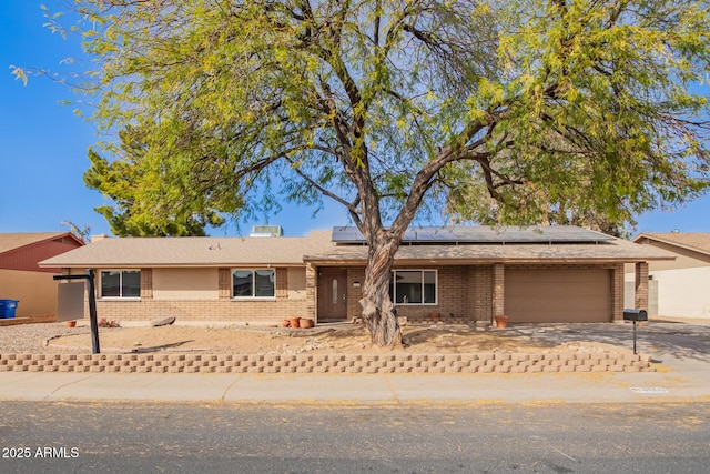 single story home featuring a garage, concrete driveway, brick siding, and solar panels