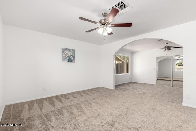 unfurnished room featuring arched walkways, visible vents, baseboards, a ceiling fan, and carpet