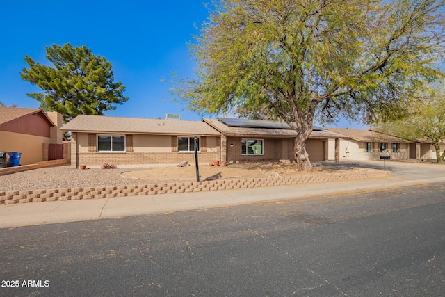 single story home with concrete driveway, brick siding, an attached garage, and solar panels