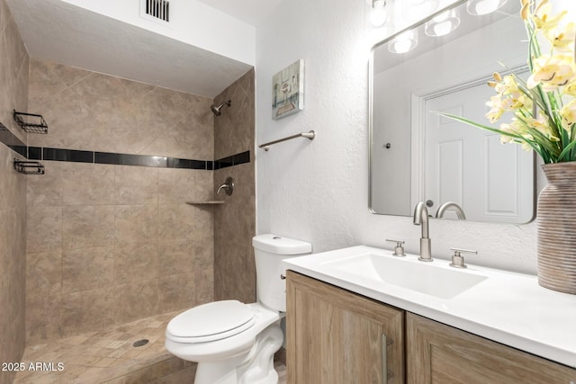 bathroom featuring visible vents, a textured wall, toilet, a tile shower, and vanity