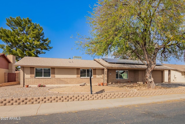 ranch-style home featuring brick siding, solar panels, fence, a garage, and driveway