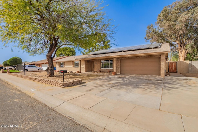 ranch-style home featuring a garage, solar panels, brick siding, fence, and a gate