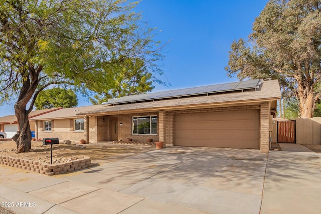 ranch-style home with a garage, solar panels, brick siding, driveway, and a gate