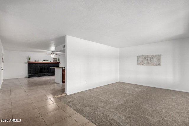 carpeted spare room with a ceiling fan, a fireplace, and tile patterned floors