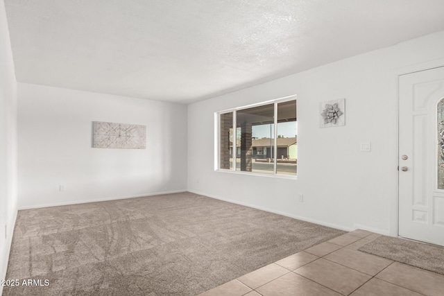 carpeted empty room with tile patterned flooring, baseboards, and a textured ceiling