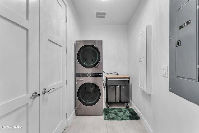 washroom featuring stacked washer and dryer, electric panel, and cabinets