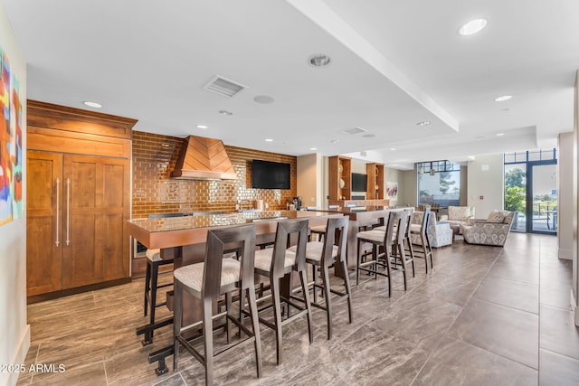 kitchen featuring custom exhaust hood, a breakfast bar area, decorative backsplash, and kitchen peninsula