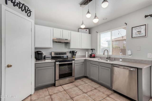 kitchen with under cabinet range hood, gray cabinetry, a sink, light countertops, and appliances with stainless steel finishes