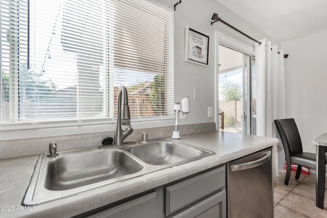 kitchen featuring light tile patterned floors, a sink, light countertops, stainless steel dishwasher, and gray cabinets