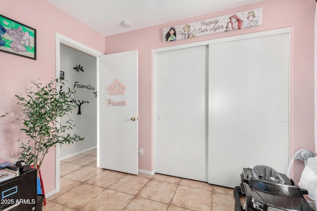 bedroom with a closet, light tile patterned flooring, and baseboards