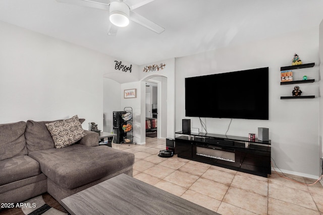 living area with light tile patterned floors, ceiling fan, arched walkways, and baseboards