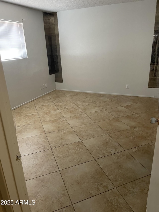 unfurnished room with light tile patterned floors, baseboards, and a textured ceiling