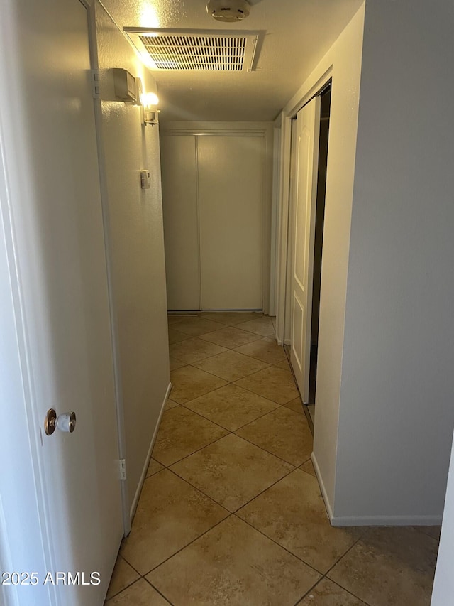 hallway featuring light tile patterned flooring, visible vents, and baseboards