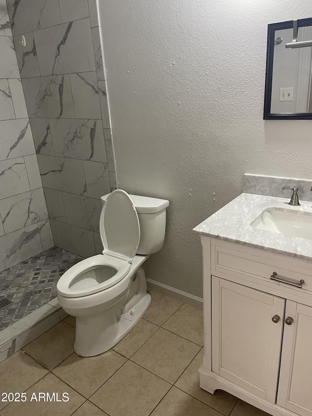 bathroom featuring a textured wall, toilet, a stall shower, vanity, and baseboards