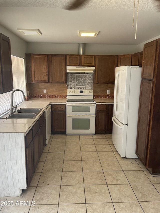 kitchen featuring light tile patterned flooring, under cabinet range hood, white appliances, a sink, and light countertops