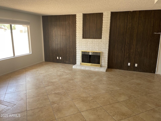 unfurnished living room with wood walls, a fireplace, a textured ceiling, and light tile patterned floors