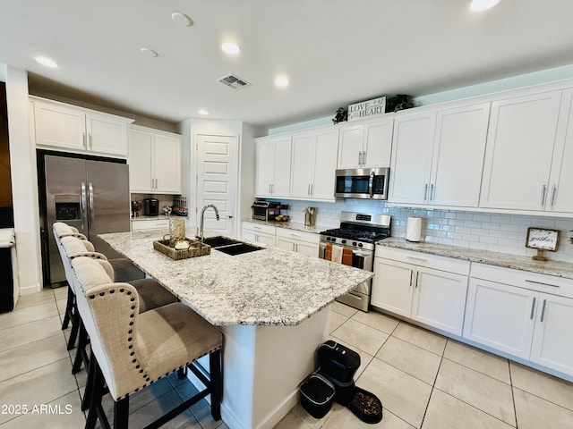 1657 W Monte Way, Phoenix, AZ 85041 - kitchen with appliances with stainless steel finishes, tasteful backsplash, light tile patterned flooring, white cabinetry, and an island with sink