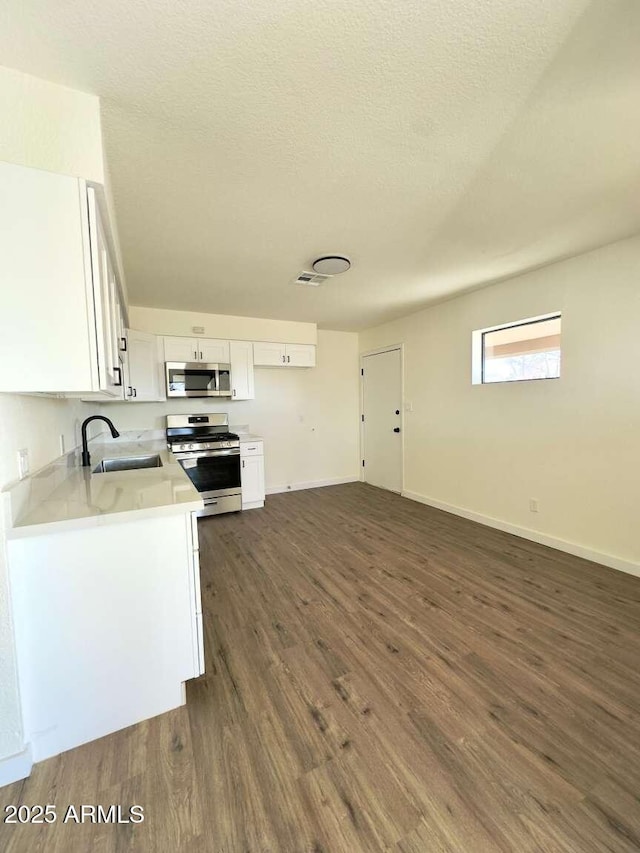 kitchen with sink, appliances with stainless steel finishes, a textured ceiling, white cabinets, and dark hardwood / wood-style flooring