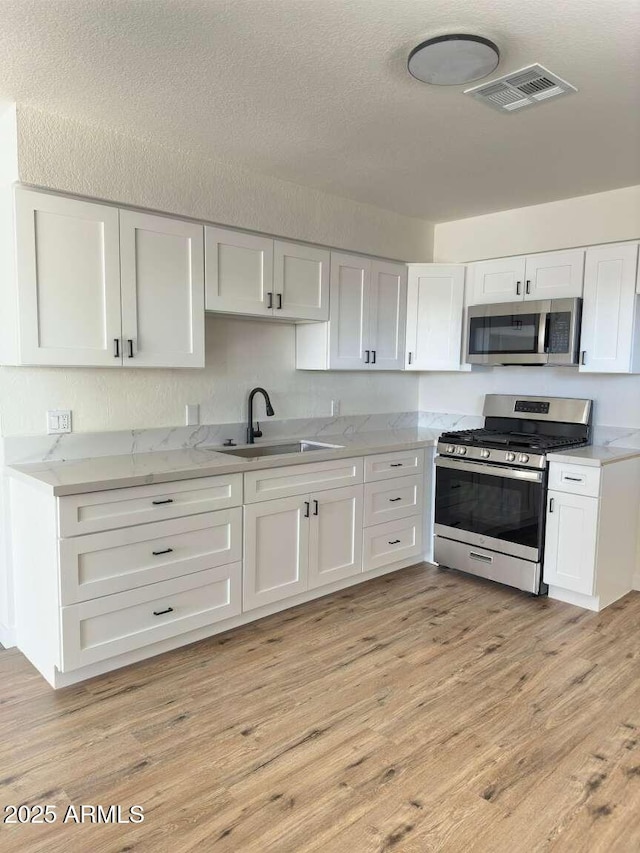 kitchen featuring white cabinetry, sink, light wood-type flooring, and appliances with stainless steel finishes