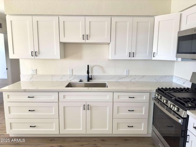 kitchen with sink, hardwood / wood-style flooring, appliances with stainless steel finishes, light stone counters, and white cabinets