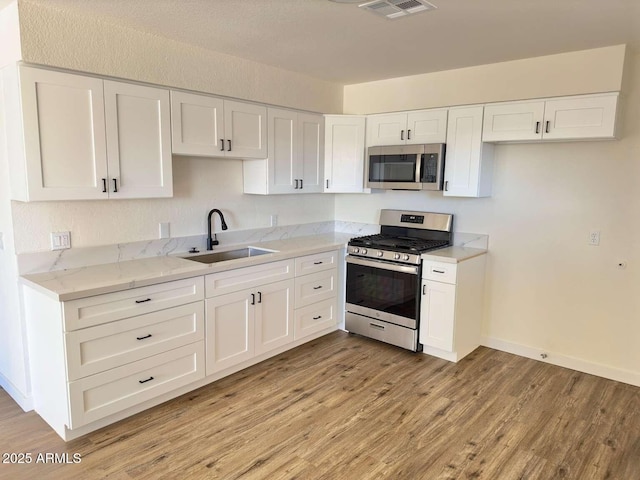 kitchen with white cabinetry, appliances with stainless steel finishes, sink, and light hardwood / wood-style flooring