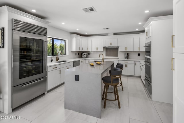 kitchen with white cabinetry, an island with sink, sink, a breakfast bar area, and beverage cooler