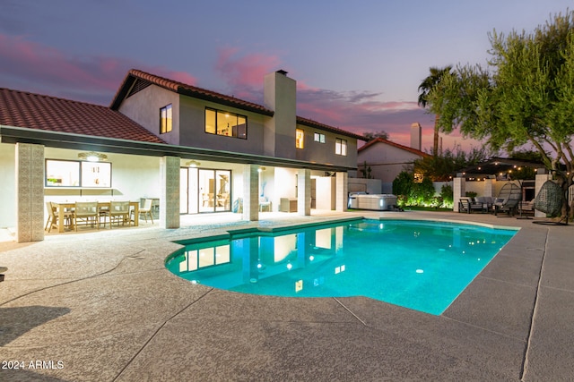 pool at dusk with a hot tub and a patio area