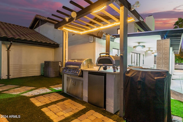 patio terrace at dusk featuring exterior kitchen, grilling area, and a pergola