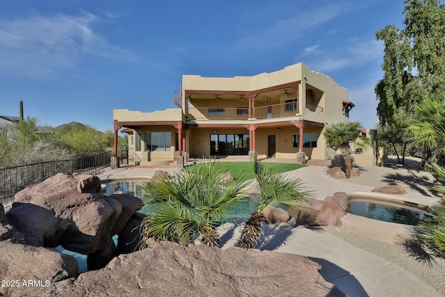 back of house featuring stucco siding, a ceiling fan, a fenced in pool, and a balcony