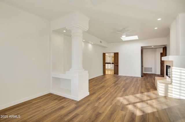 unfurnished living room featuring decorative columns, visible vents, baseboards, a glass covered fireplace, and wood finished floors