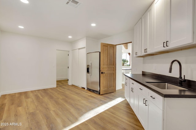 kitchen featuring light wood-style flooring, a sink, stainless steel fridge, dark countertops, and visible vents