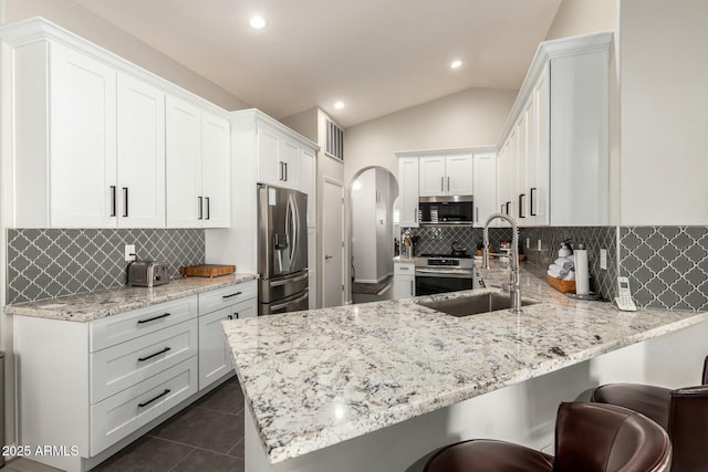 kitchen with vaulted ceiling, kitchen peninsula, stainless steel appliances, and white cabinets