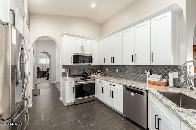 kitchen with light stone countertops, white cabinets, appliances with stainless steel finishes, lofted ceiling, and tasteful backsplash