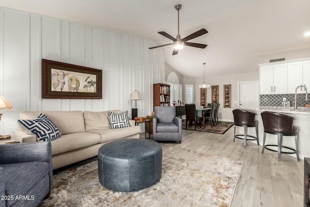 living room with ceiling fan, lofted ceiling, sink, and light hardwood / wood-style flooring