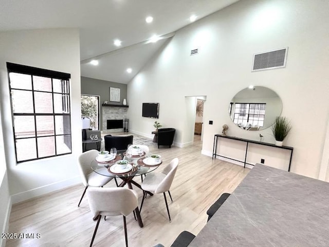 dining room featuring a fireplace, high vaulted ceiling, plenty of natural light, and light wood-type flooring