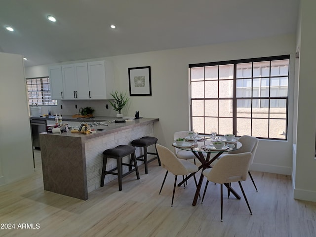 kitchen featuring a kitchen bar, kitchen peninsula, stainless steel dishwasher, light hardwood / wood-style flooring, and white cabinets