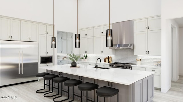 kitchen featuring a sink, ventilation hood, built in appliances, light wood-style flooring, and a towering ceiling